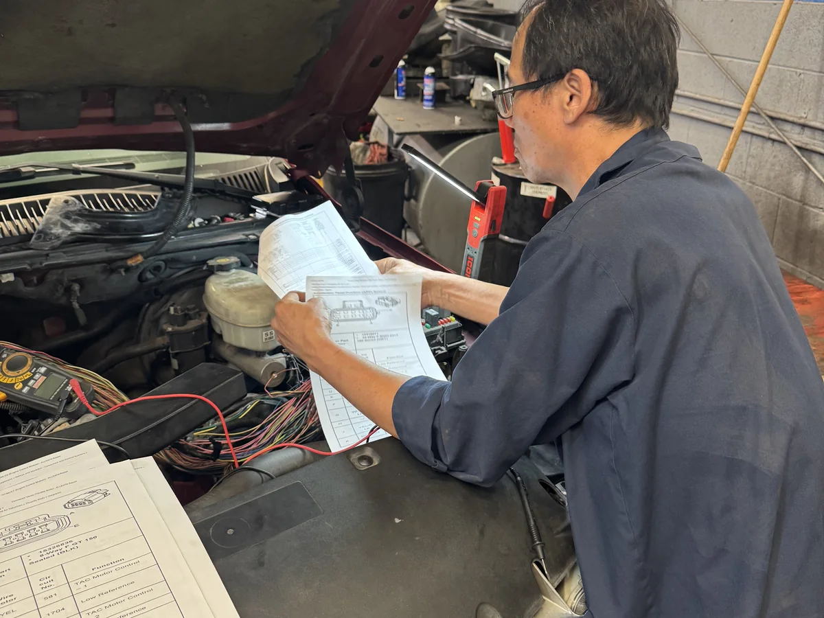 Allen’s Automotive mechanic inspecting vehicle wiring under the hood with diagrams and a multimeter